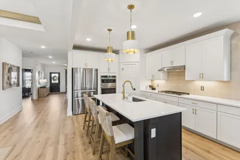 a open kitchen with stainless steel appliances granite countertop a stove a sink a refrigerator and white cabinets with wooden floor