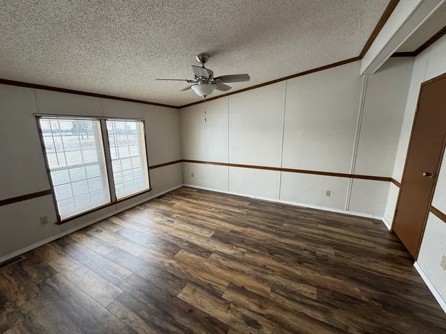 a view of an empty room with wooden floor and fan