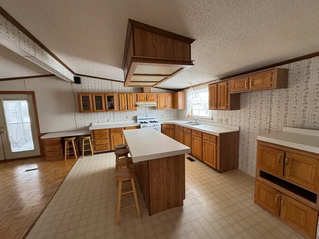 a open kitchen with stainless steel appliances kitchen island granite countertop a stove a sink dishwasher and white cabinets with wooden floor