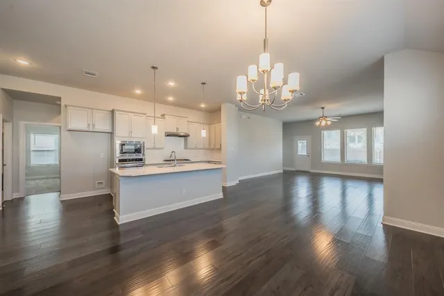 a large kitchen with kitchen island a sink dishwasher a refrigerator and white cabinets with wooden floor