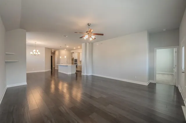 a view of an empty room with wooden floor and a ceiling fan