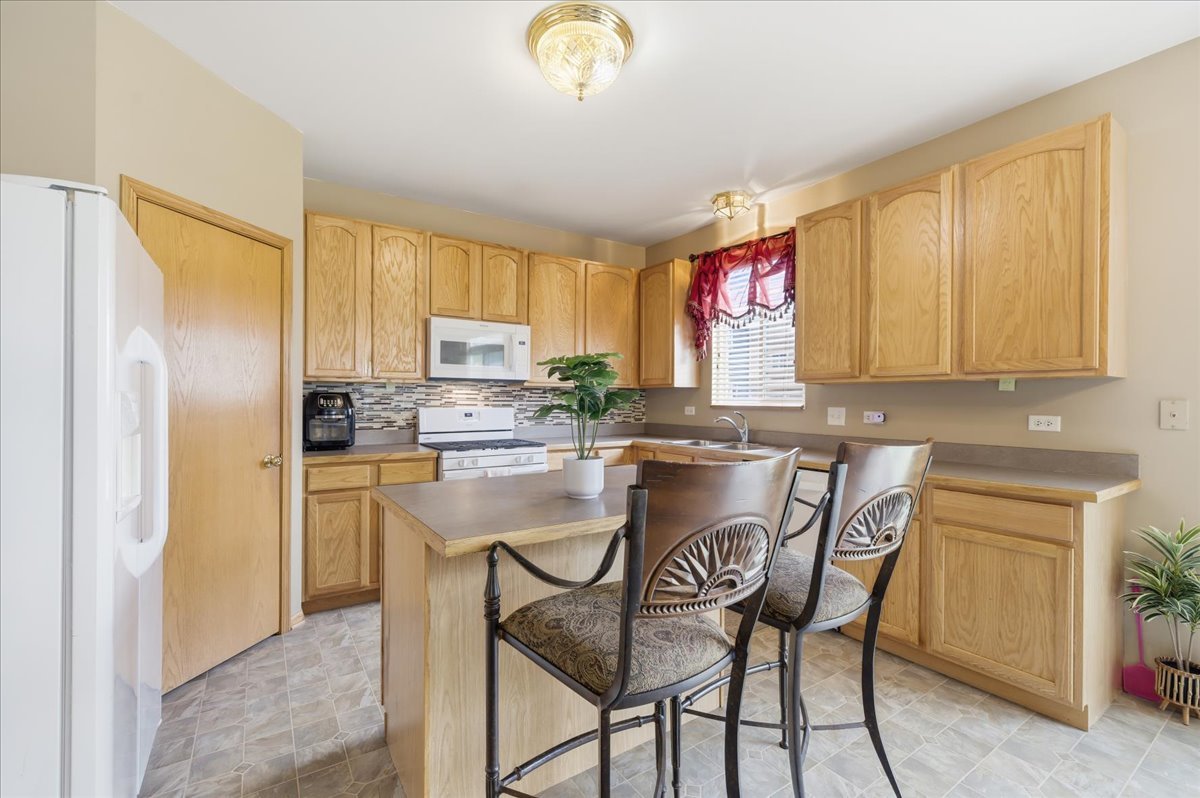 1916 Castle Ridge Drive Plainfield, IL 60586 - Photo 13 of 36 a kitchen with a refrigerator a stove a kitchen island and chairs with wooden floor