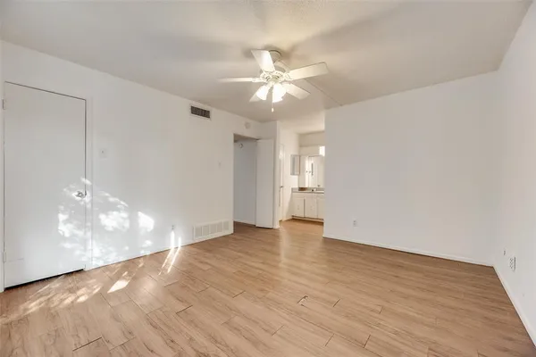 a view of an empty room with wooden floor and a ceiling fan