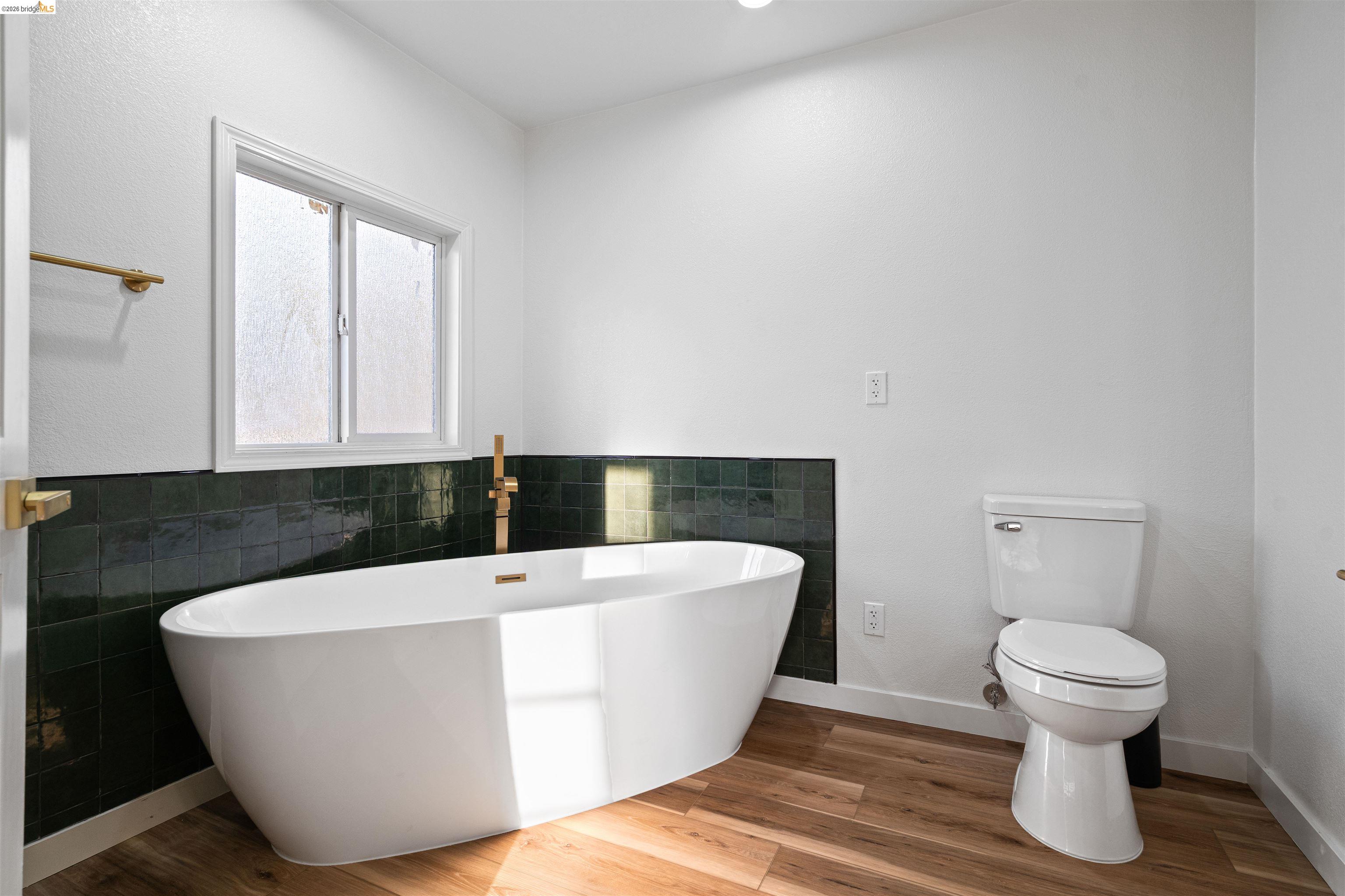 19676 Rawhide Road Sonora, CA 95370 - Photo 31 of 67 Freestanding soaking tub with a wall-mounted brass faucet, wood-finish flooring, and white walls