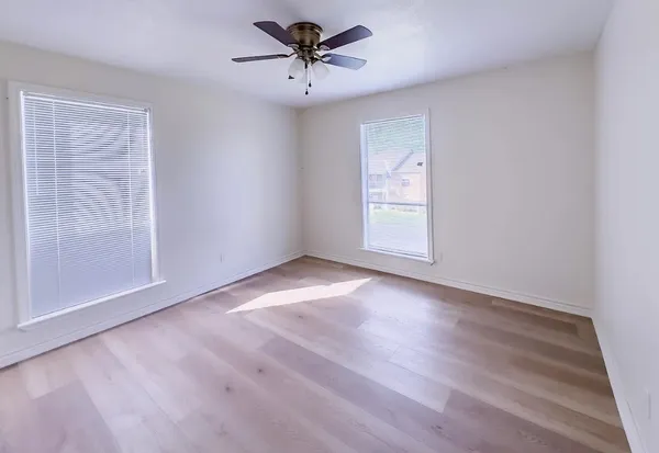 an empty room with wooden floor chandelier fan and windows
