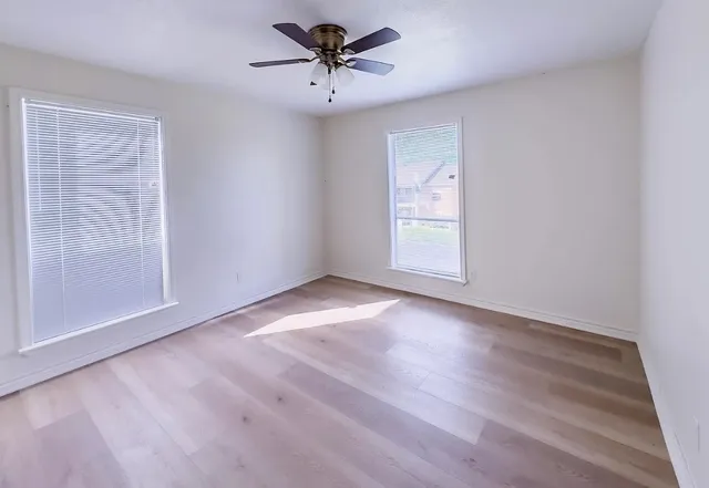 an empty room with wooden floor chandelier fan and windows