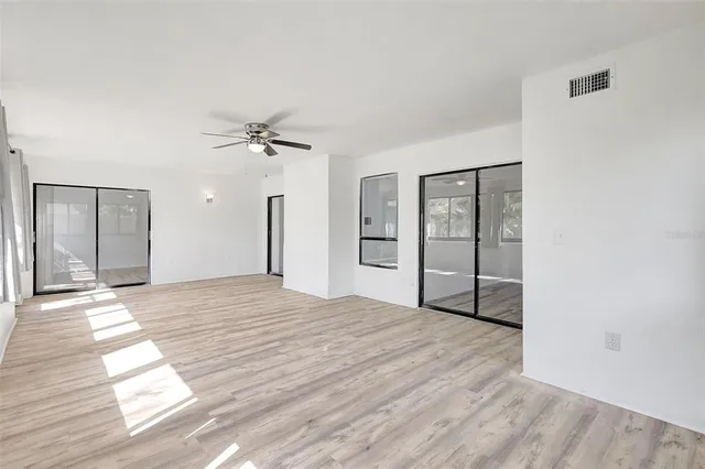 an empty room with wooden floor fan and windows
