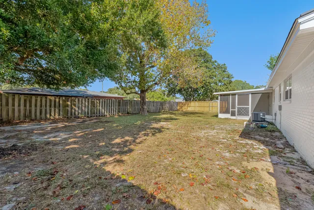 a backyard of a white house with large tree and wooden fence