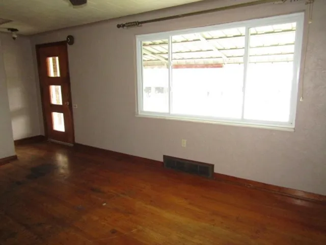 a view of an empty room with wooden floor and a window