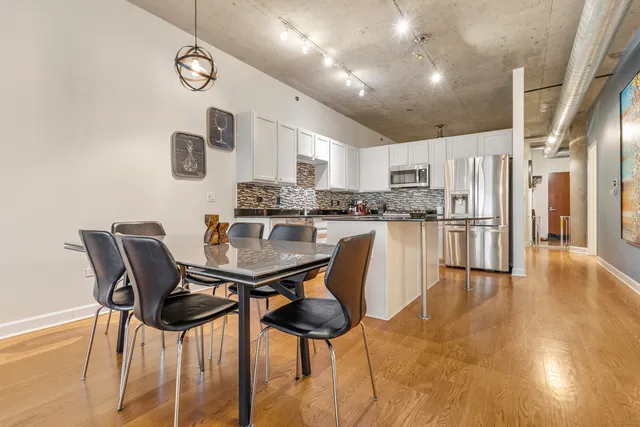 a kitchen with stainless steel appliances kitchen island granite countertop a dining table chairs and a refrigerator