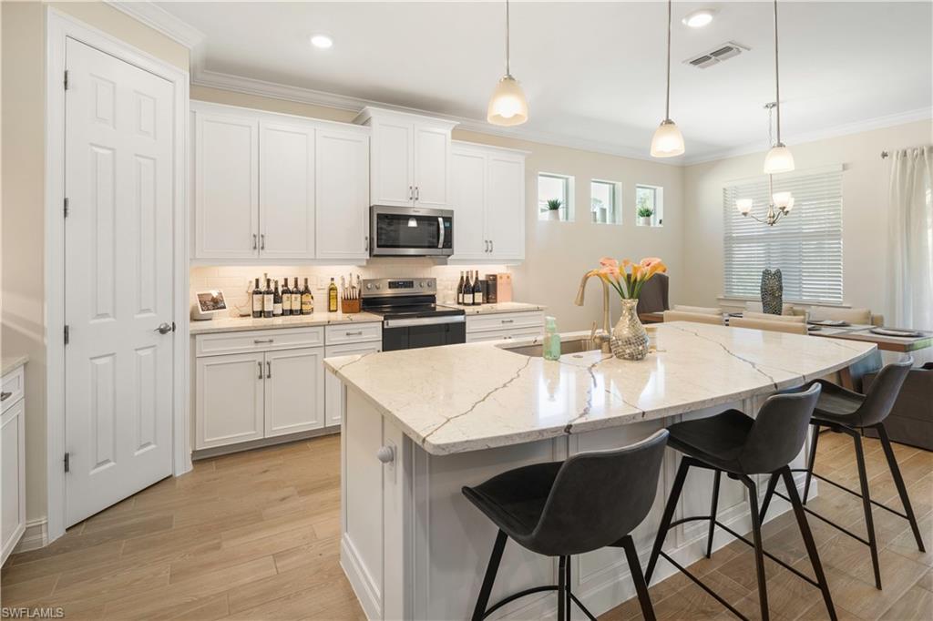 329 Deauville Loop Naples, FL 34114 - Photo 3 of 22 a kitchen with stainless steel appliances kitchen island granite countertop a sink a stove a dining table and chairs