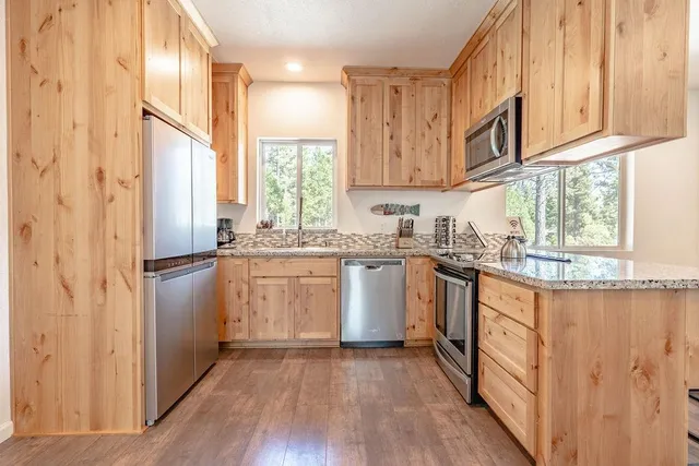 a kitchen with stainless steel appliances granite countertop a refrigerator a sink dishwasher a stove and white countertops with wooden floor