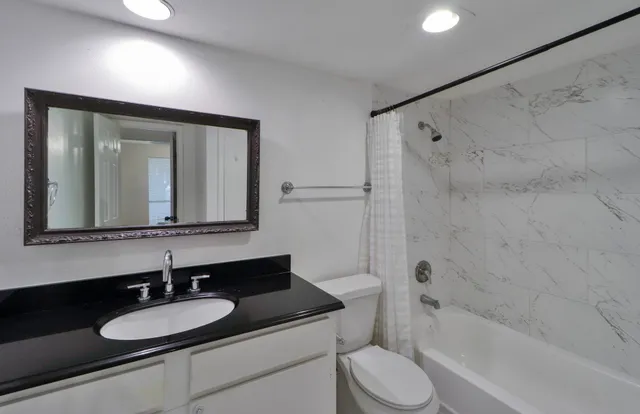 a bathroom with a granite countertop sink toilet a mirror and shower