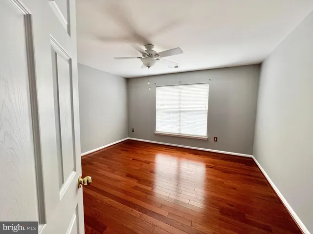 an empty room with wooden floor ceiling fan and windows