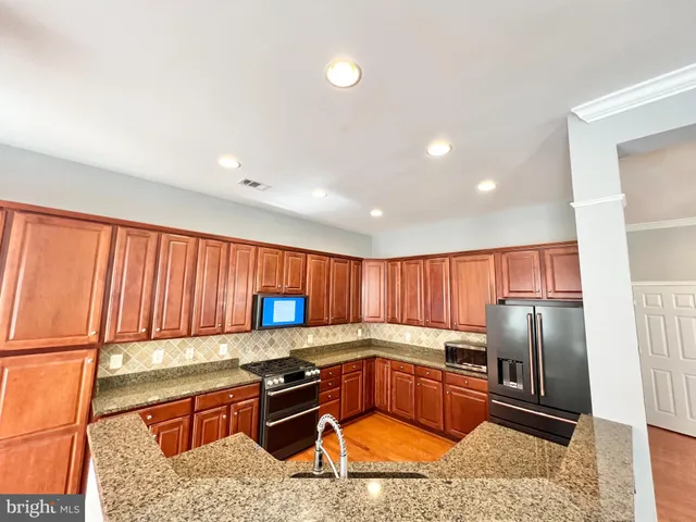 a kitchen with stainless steel appliances granite countertop a refrigerator a sink a stove and blue cabinets with wooden floor