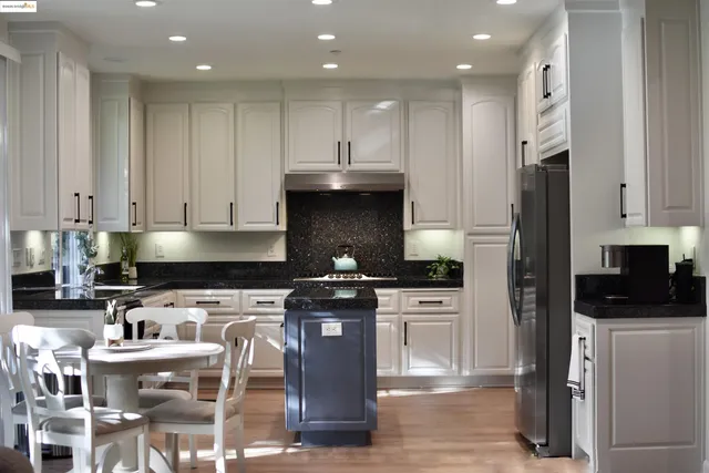 a kitchen with stainless steel appliances granite countertop a stove top oven a sink a refrigerator and white cabinets