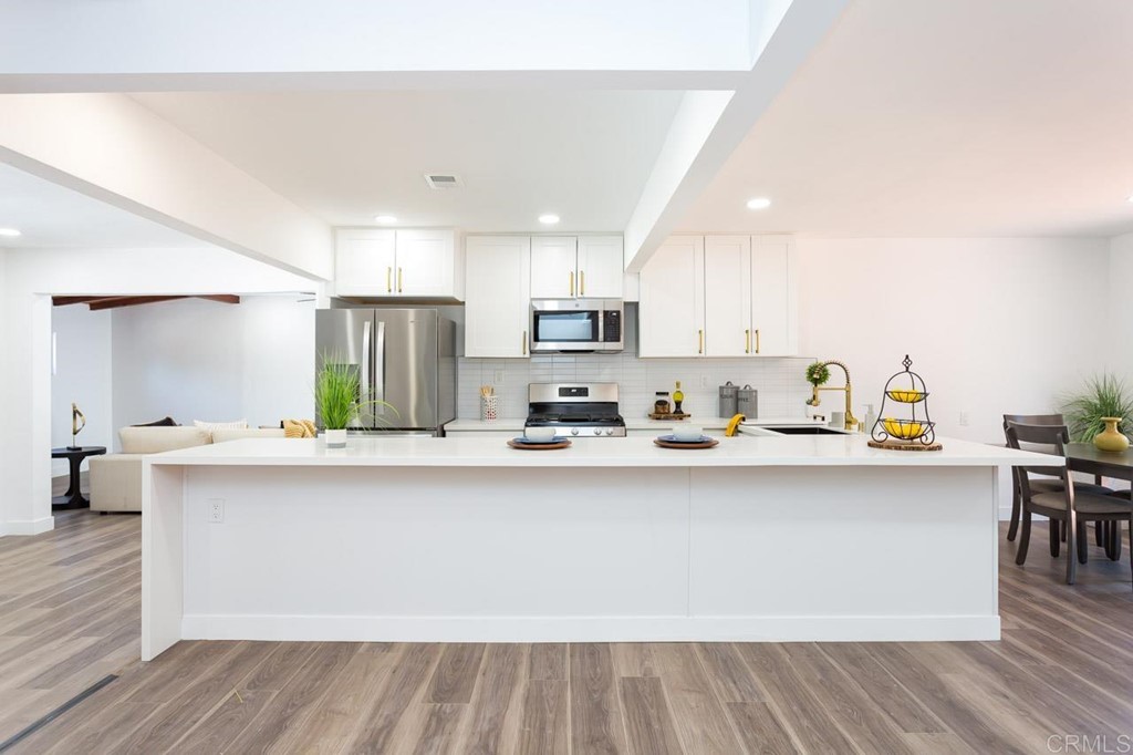 a kitchen with stainless steel appliances a sink a stove a refrigerator cabinets and a dining table with wooden floor