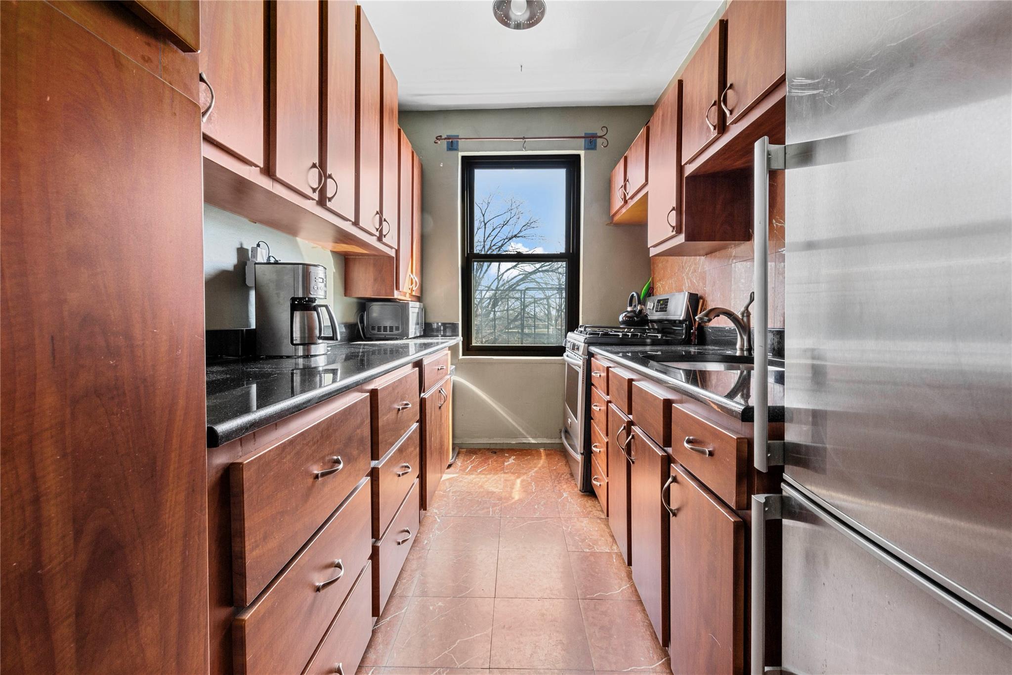 Kitchen featuring dark countertops, appliances with stainless steel finishes, a sink, backsplash, and light tile patterned floors