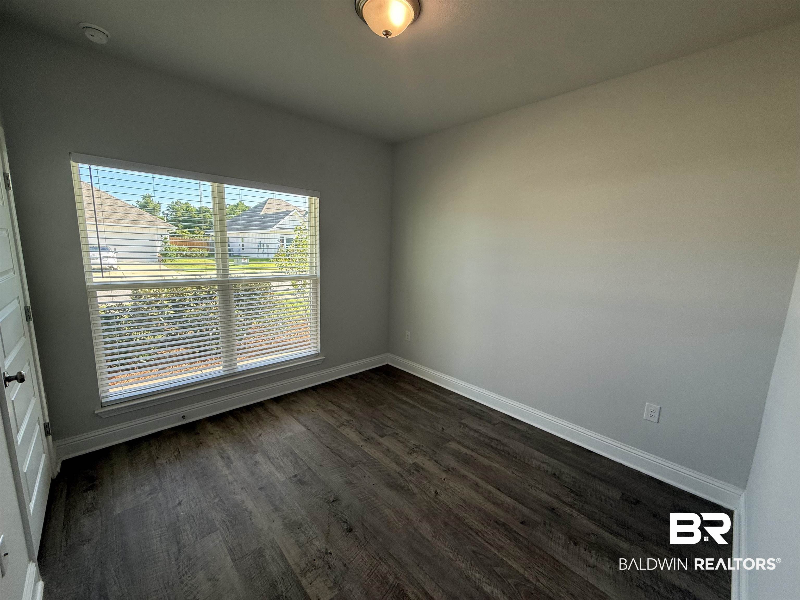 23247 Lieutenant Avenue Foley, AL 36535 - Photo 6 of 47 Room featuring wood-finish flooring, a double-paned window with blinds, light gray wall paint, white baseboards, and a flush-mount ceiling light