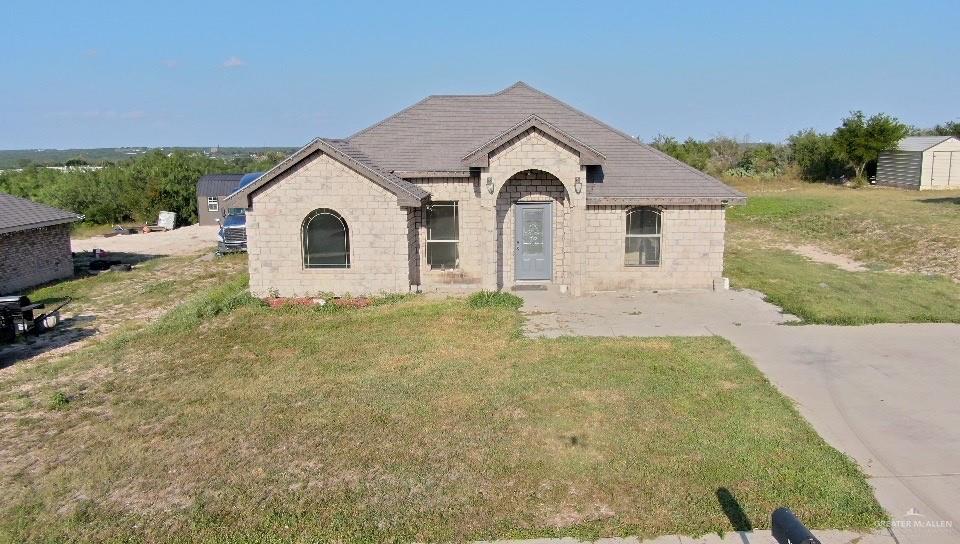 311 Teodora Drive Rio Grande City, TX 78582 - Photo 1 of 15 French country style house featuring stone siding, a storage shed, and a front yard