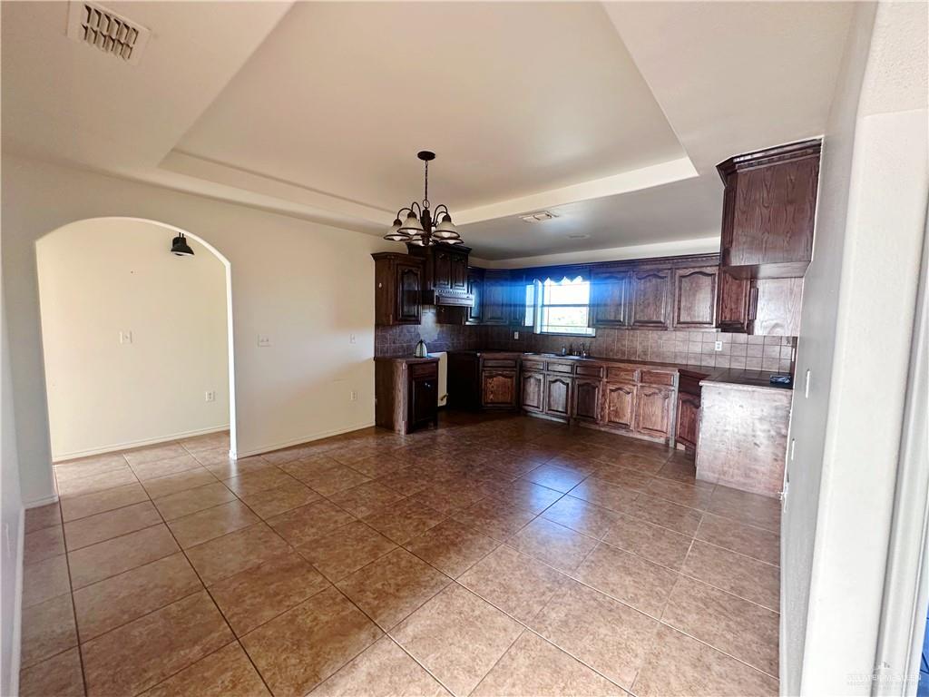 311 Teodora Drive Rio Grande City, TX 78582 - Photo 3 of 15 Kitchen with a raised ceiling, tasteful backsplash, dark tile patterned floors, arched walkways, and a chandelier