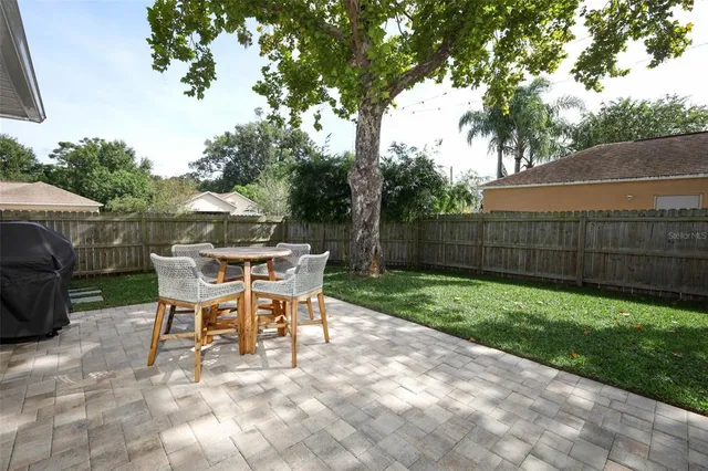 a view of a backyard with table and chairs potted plants and a large tree