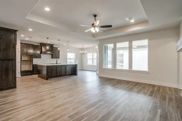 a view of an empty room with wooden floor and a kitchen
