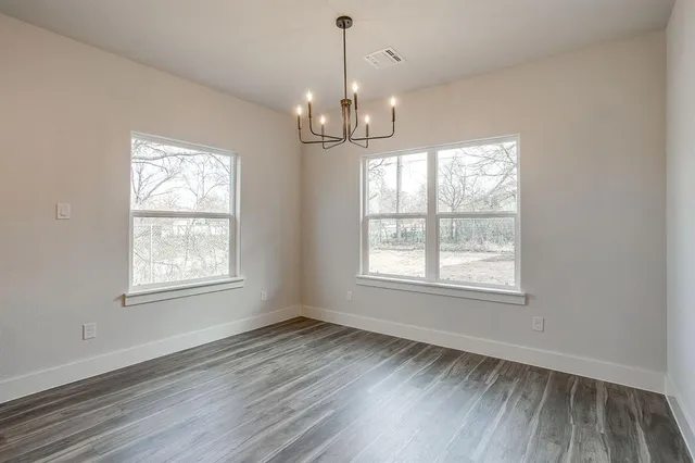 an empty room with wooden floor chandelier and windows