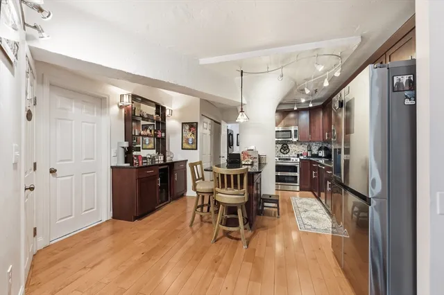 a kitchen with stainless steel appliances a refrigerator a stove a dining table and chairs with wooden floor