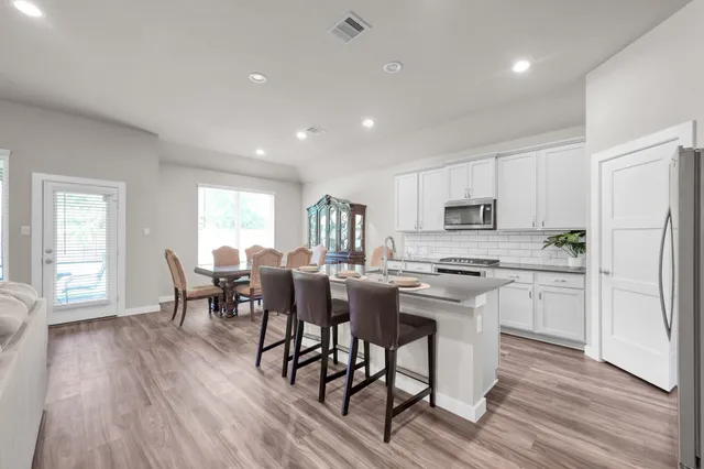 a kitchen with stainless steel appliances granite countertop a stove a refrigerator a microwave a dining table and chairs with wooden floor