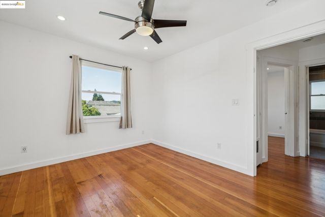 an empty room with wooden floor ceiling fan and windows