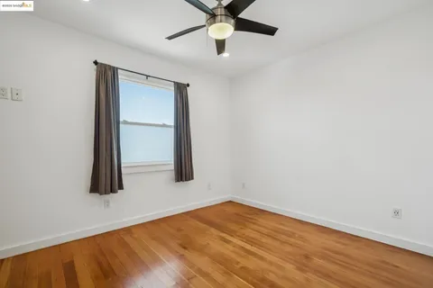 a view of an empty room with wooden floor and a ceiling fan