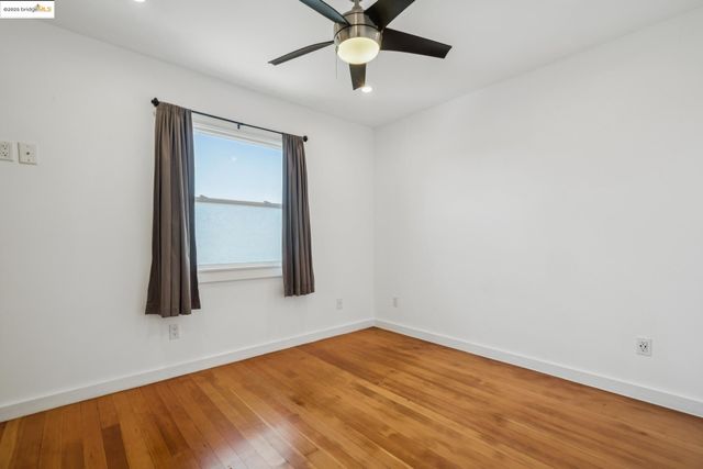 a view of an empty room with wooden floor and a ceiling fan