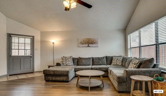 Living area featuring wood-finish flooring, vaulted ceiling, and a ceiling fan with light fixture