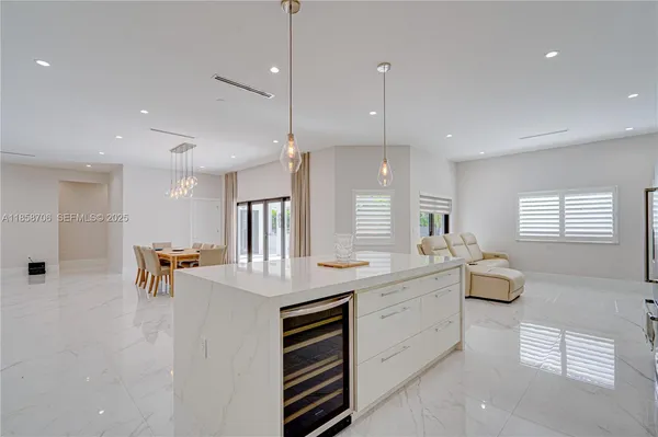 a large white kitchen with kitchen island granite countertop a stove a sink a dining table and chairs with wooden floor