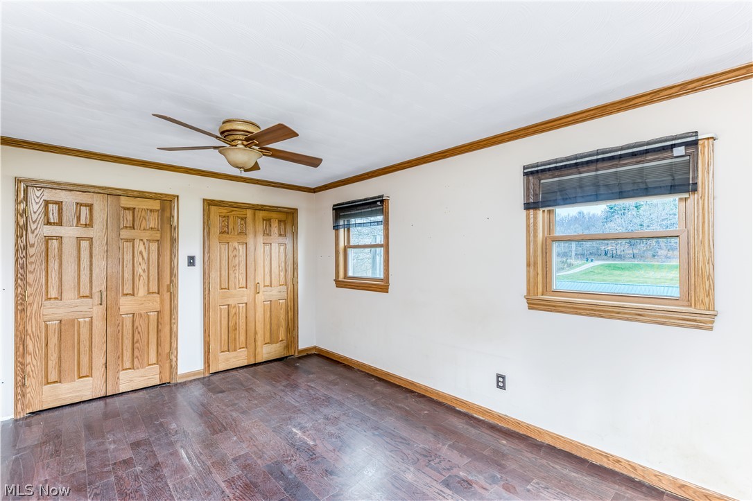 8750 Whitaker Road Cambridge, OH 43725 - Photo 13 of 29 Unfurnished bedroom with ceiling fan, ornamental molding, two closets, and dark wood-type flooring