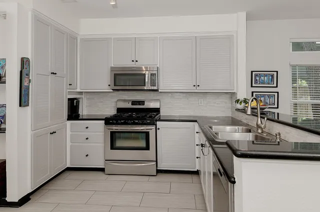 a kitchen with stainless steel appliances granite countertop a sink stove refrigerator and white cabinets