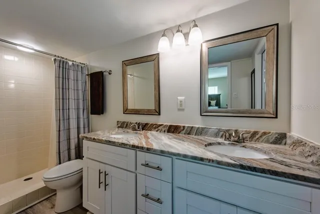 a bathroom with a granite countertop sink vanity mirror shower and a toilet