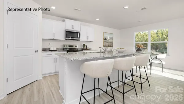 a kitchen with stainless steel appliances granite countertop a stove top oven a sink a refrigerator and white cabinets with wooden floor