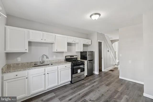a kitchen with a sink dishwasher a refrigerator and white cabinets with wooden floor