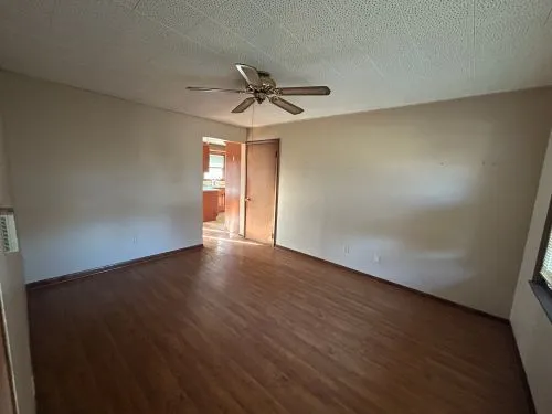 an empty room with wooden floor ceiling fan and windows