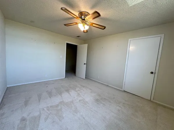 an empty room with chandelier fan and windows