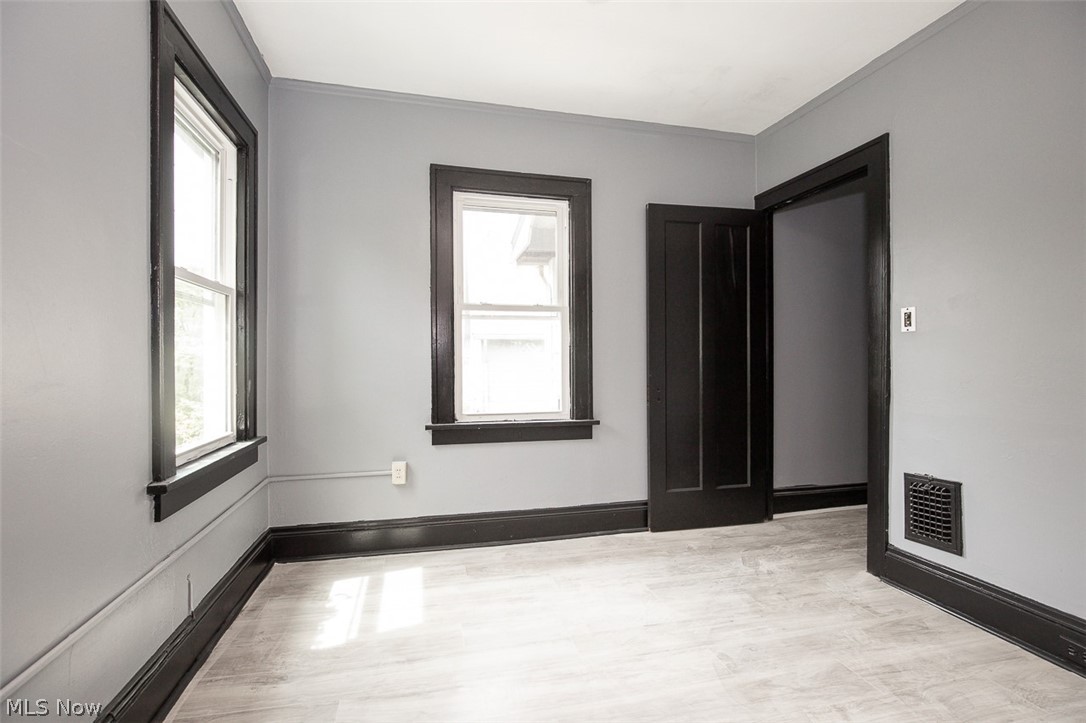 1868-1870 Lampson Road Cleveland, OH 44112 - Photo 19 of 36 Room featuring light wood-finish flooring, two large windows with dark trim, a dark paneled door, and a wall vent