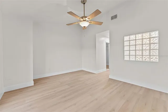 an empty room with wooden floor fan and windows