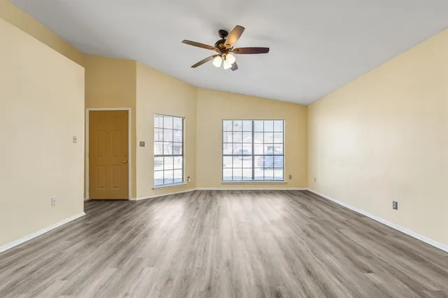an empty room with wooden floor chandelier fan and windows
