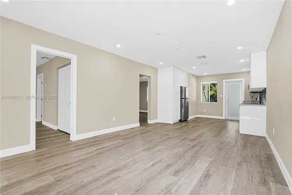 a view of an empty room with wooden floor and a kitchen