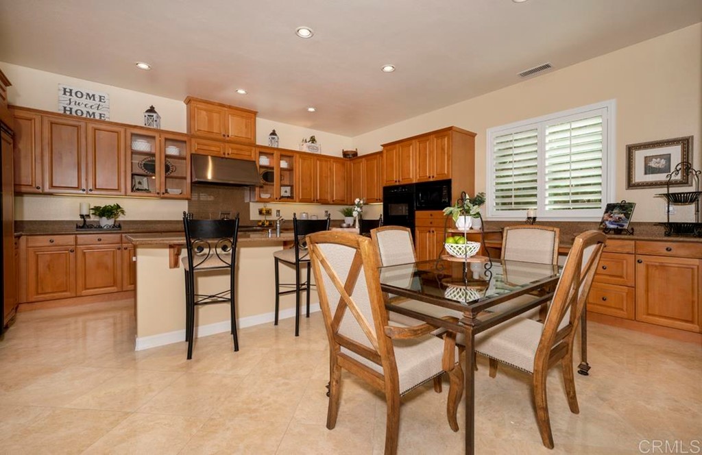 2887 Rancho Cortes Carlsbad, CA 92009 - Photo 25 of 46 a kitchen with stainless steel appliances kitchen island granite countertop a dining table chairs and a refrigerator