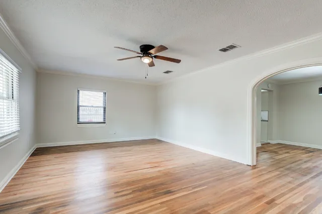 an empty room with wooden floor chandelier fan and windows