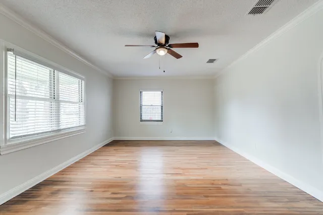 an empty room with wooden floor ceiling fan and windows
