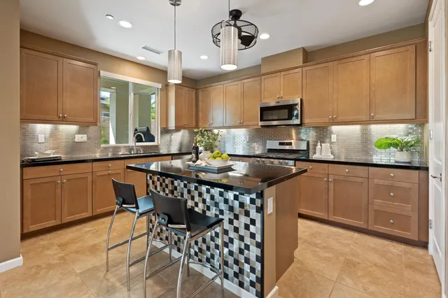a kitchen with stainless steel appliances granite countertop a kitchen island a stove a refrigerator a sink a dining table and chairs with wooden floor